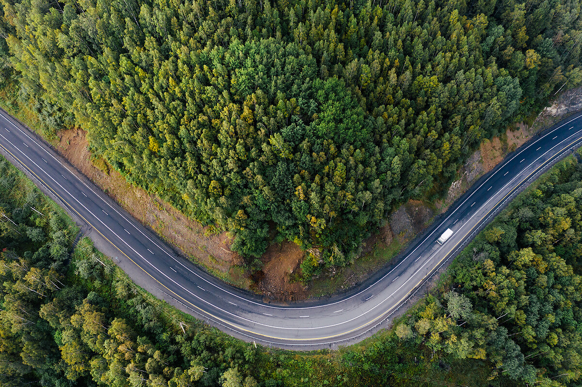 Top down aerial view of mountain road curve among green forest trees.
