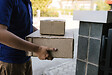 Asian cargo carrier holds a cardboard box with the package inside and the recipient is signing the package.