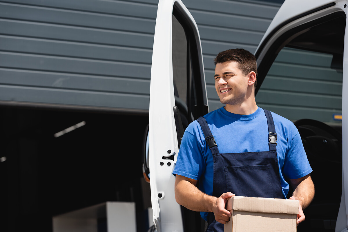 Loader holding cardboard box and looking away near truck outdoors