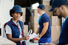 Smiling black delivery woman taking notes while talking to her coworker.